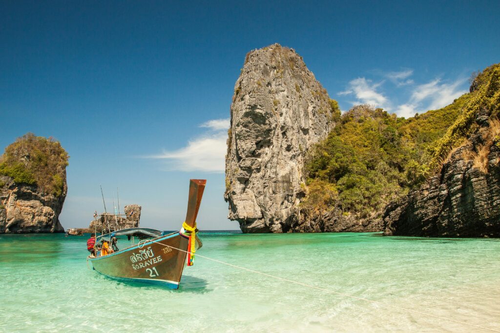 A picturesque tropical beach with a traditional boat and stunning limestone cliffs in clear turquoise waters.