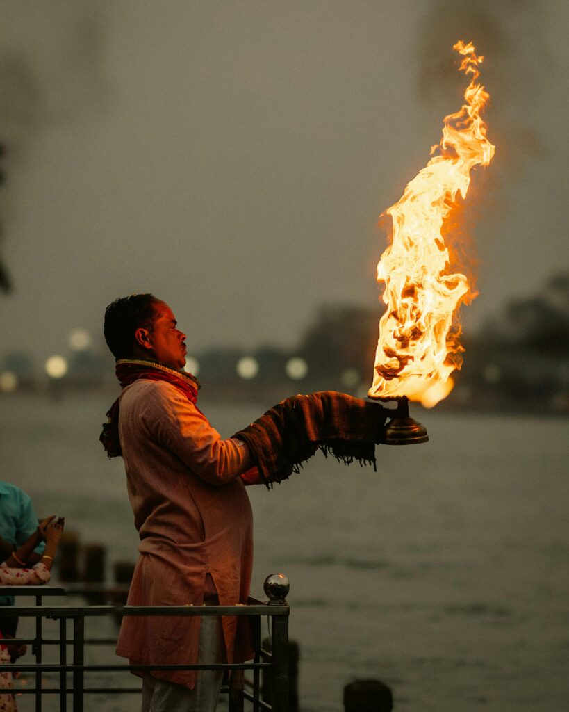 A man in traditional attire performs a fire ritual by the Ganges River in Rishikesh, India.