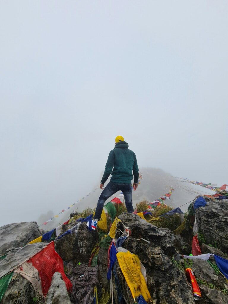 Man standing on misty Mussorie Range peak with colorful prayer flags, perfect for adventure themes.