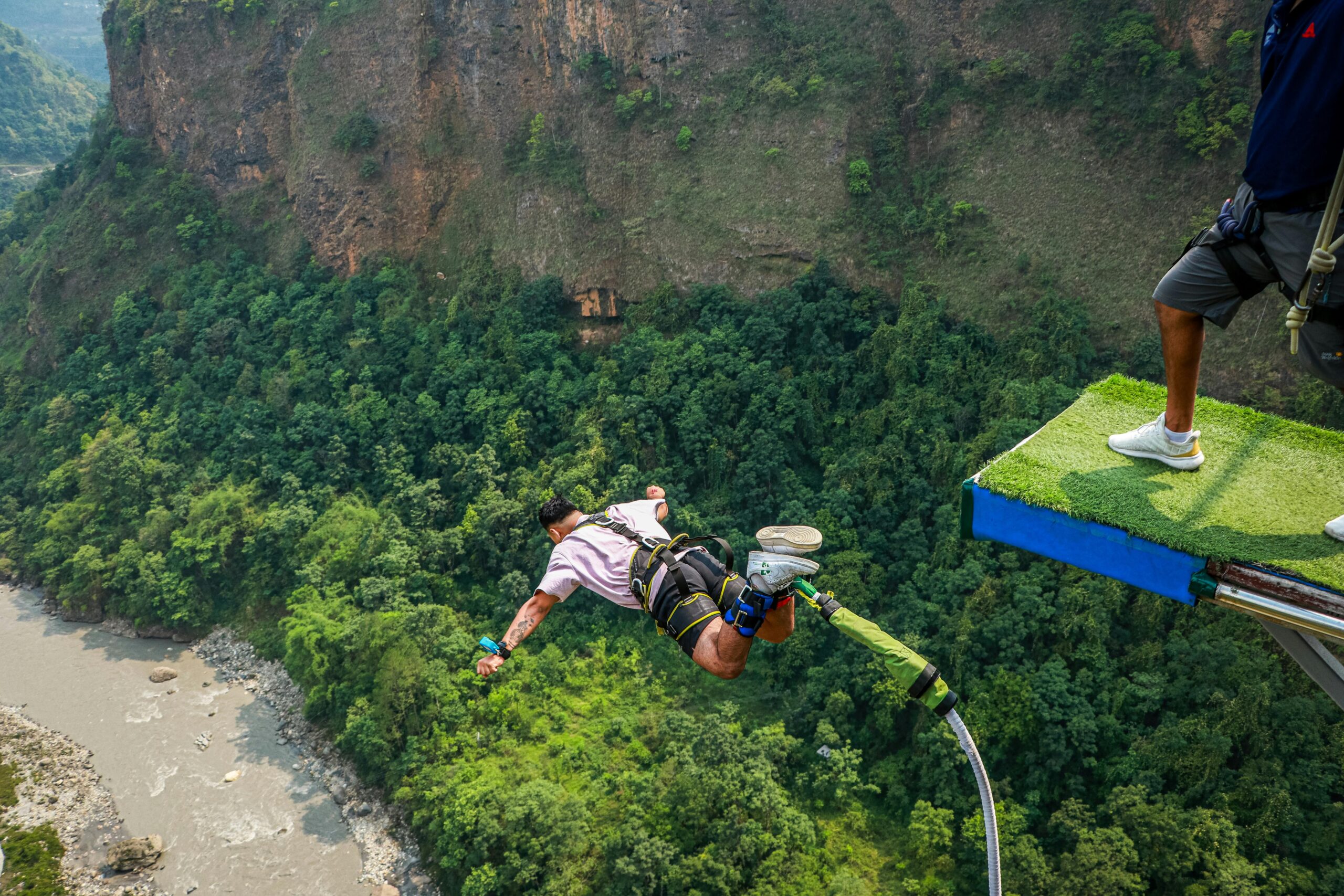 Experience the adrenaline rush of bungee jumping over a scenic canyon with dense greenery.