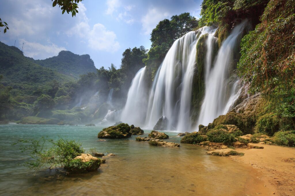 Majestic view of Ban Gioc Waterfall cascading into a serene pool amidst lush greenery in Cao Bang, Vietnam.