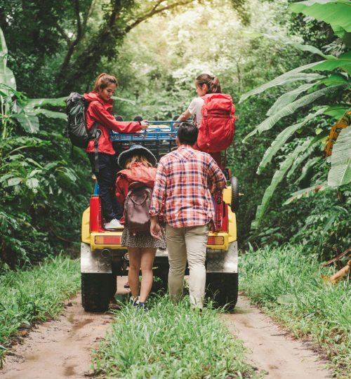 Friends hiking in a tropical forest, riding a jeep with backpacks, enjoying the adventure.